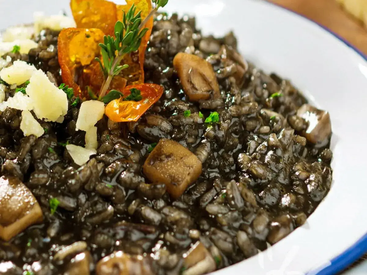 Risotto cremoso al nero di seppia, guarnito con scaglie di formaggio, pomodorini secchi e un rametto di timo.