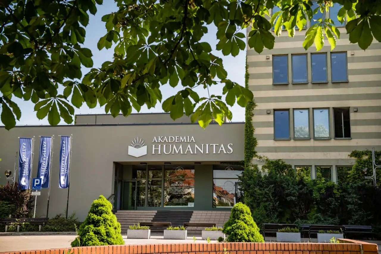 Akademia Humanitas wita studentów. Zielone drzewa i ławki przed budynkiem zachęcają do nauki.