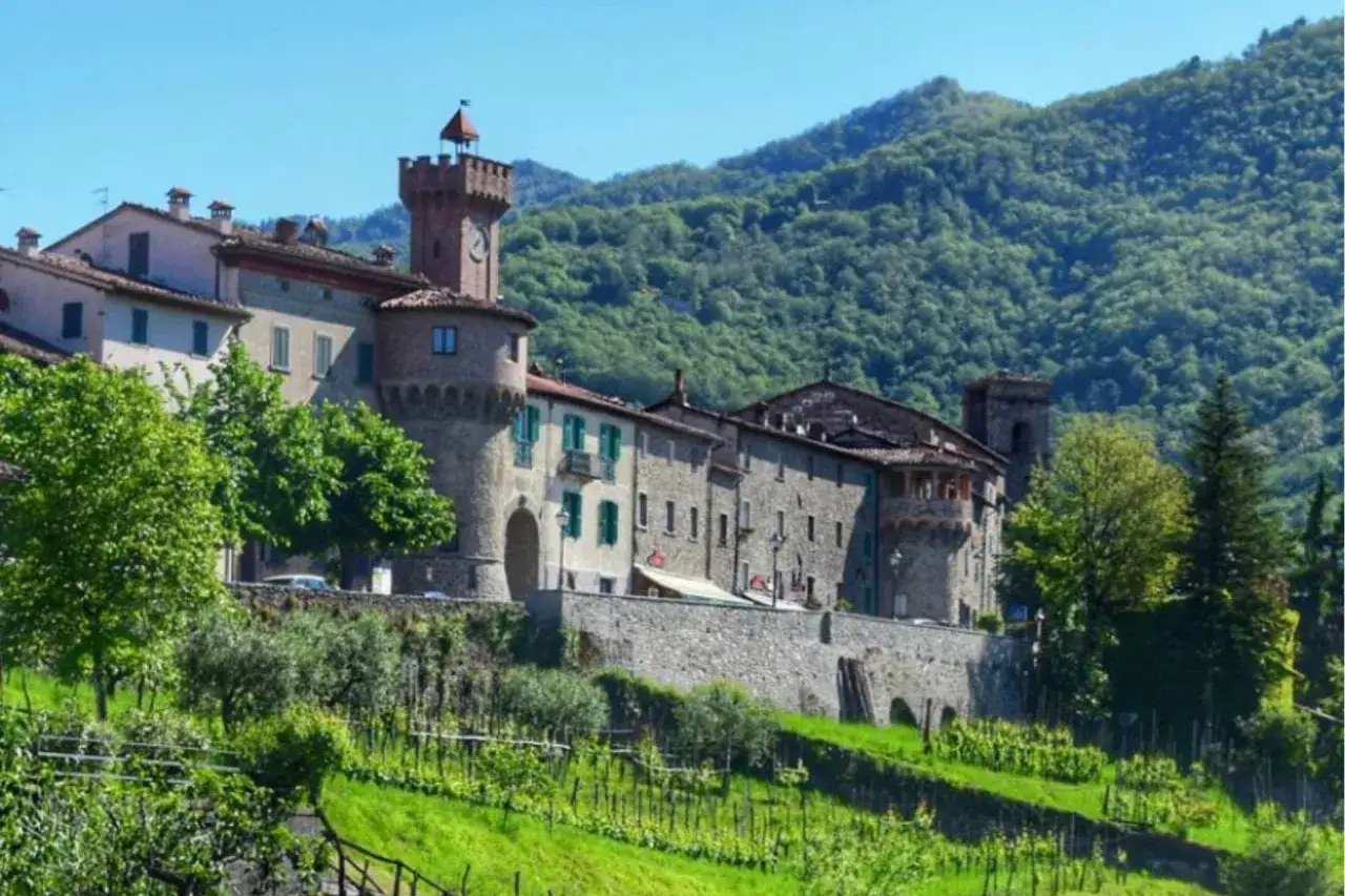 Borgo medievale di Castiglione di Garfagnana con torre dell'orologio e vigneti rigogliosi.