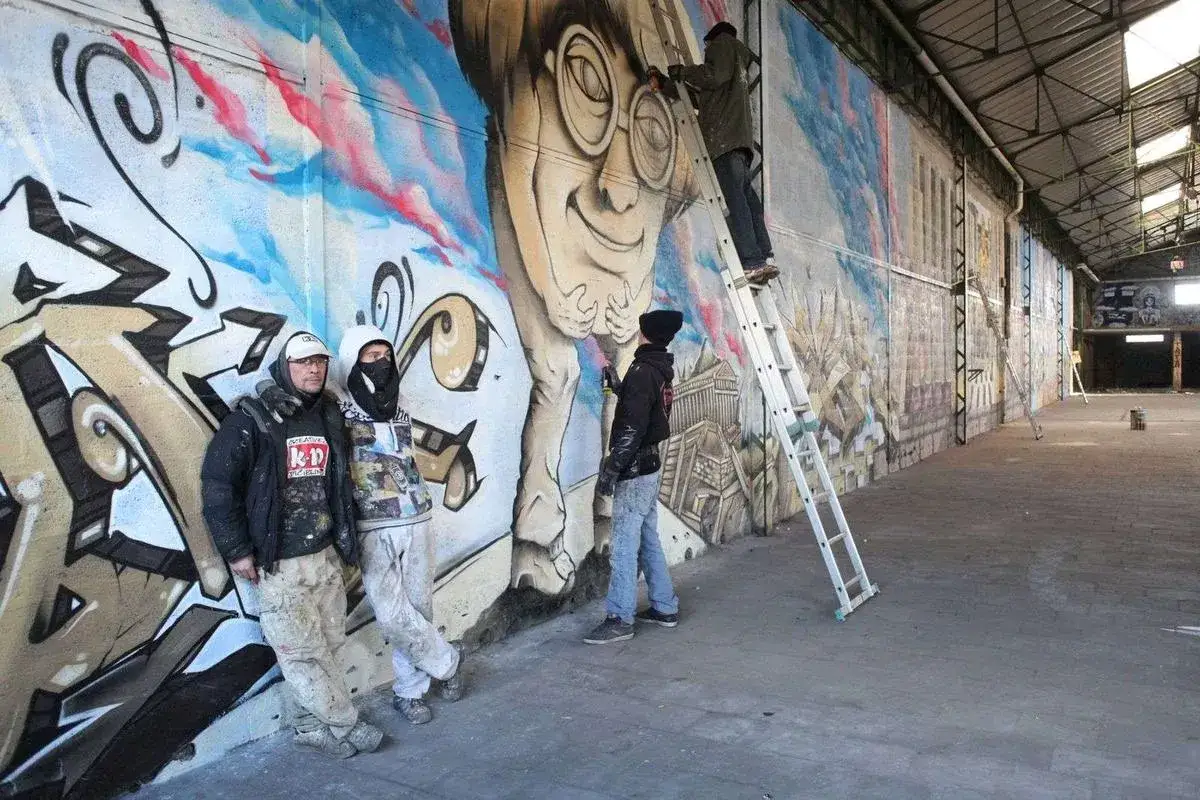 Artistes en pleine création d'une fresque murale dans un entrepôt abandonné, une scène typique d'urbex à Angoulême.