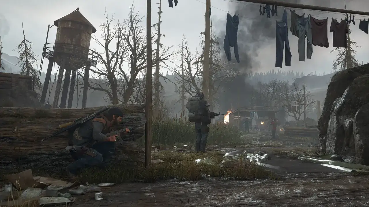 Dwóch mężczyzn z bronią w postapokaliptycznym świecie. W tle płonący budynek i suszące się ubrania. Gra Days Gone wymaga odpowiedniego sprzętu.