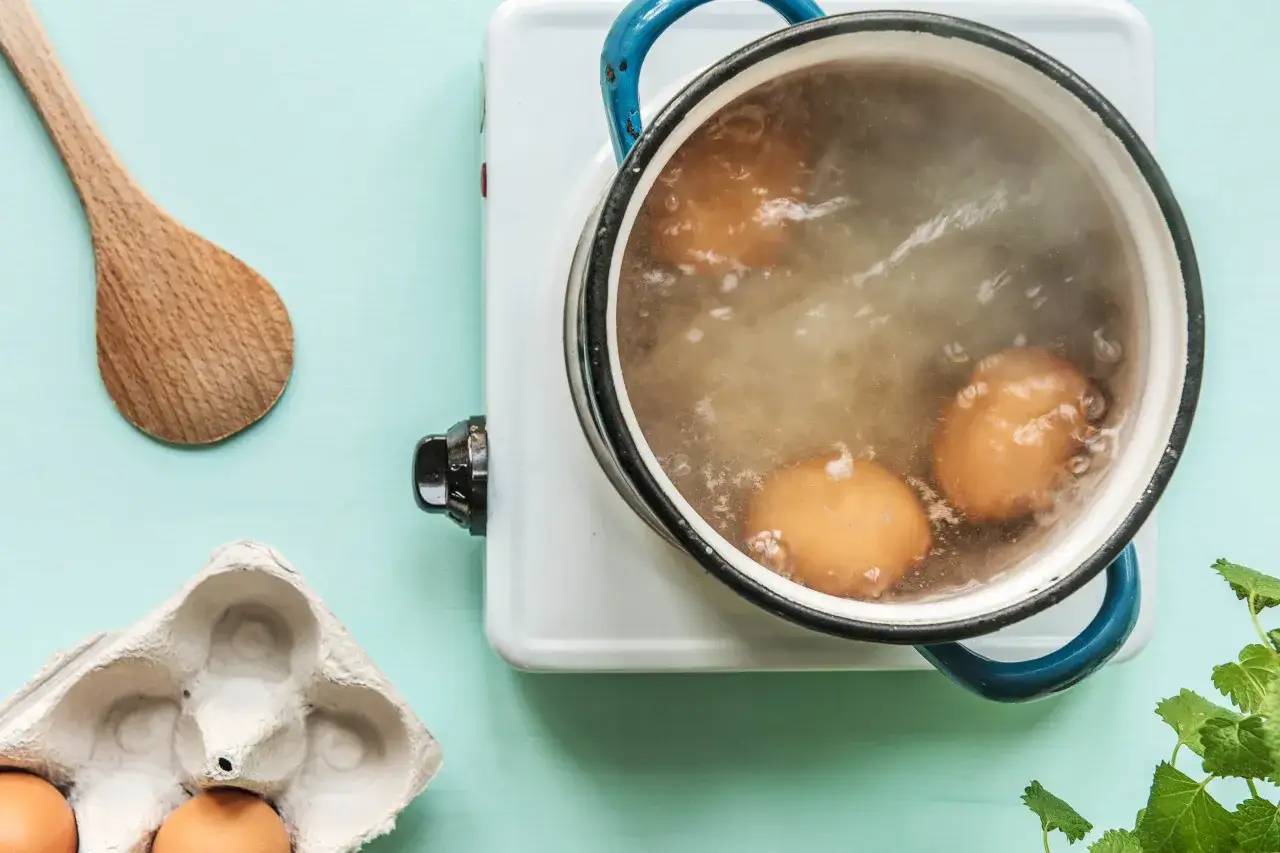 &OElig;ufs en cuisson dure dans une casserole bouillante. Une cuill&egrave;re en bois et une bo&icirc;te &agrave; &oelig;ufs sont &agrave; proximit&eacute;.