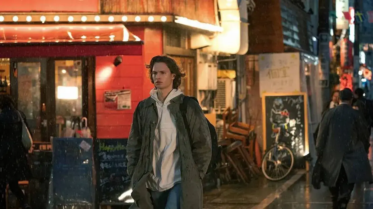 Ein junger Mann geht im Regen durch eine beleuchtete Stra&szlig;e in Tokio. Die Szene erinnert an die Atmosph&auml;re von Tokyo Vice Staffel 2.