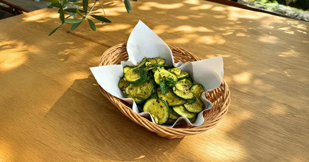Zucchine alla scapece in un cestino di vimini, condite con menta fresca e aglio, su un tavolo di legno illuminato dal sole.