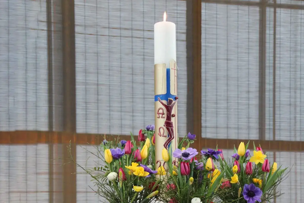 Osterkerze mit Kreuzigungssymbol und Fr&uuml;hlingsblumen. Was ist an Ostersonntag passiert? Die Auferstehung!