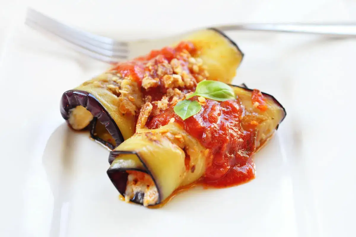 Deliziosi involtini di melanzane alla siciliana, ripieni e conditi con sugo rosso e basilico fresco, pronti per essere gustati.