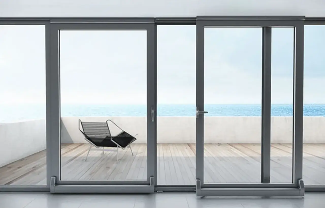 Ventanas osciloparalelas con vista al mar. Una silla de dise&ntilde;o en la terraza de madera.