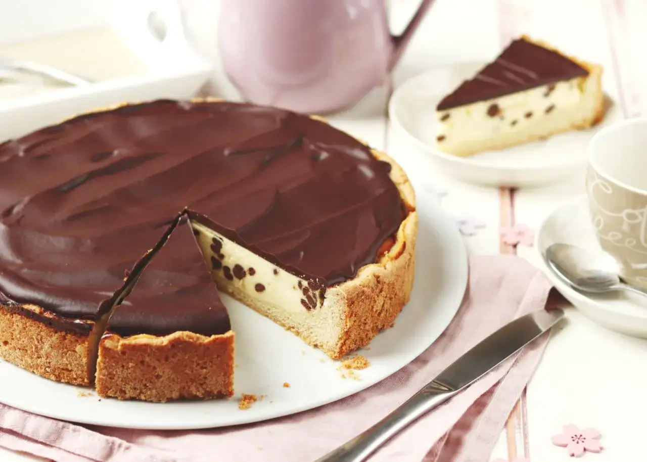 Eine köstliche Schoko Torte mit cremigem Käsekuchen-Füllung und dunkler Schokoladenglasur. Ein Stück ist bereits angeschnitten.