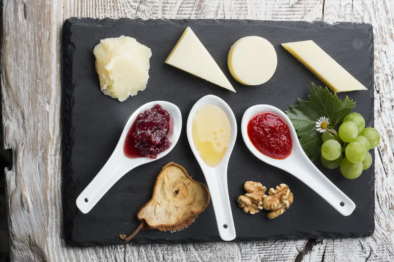 Assortimento di formaggi con diverse marmellate, miele, frutta secca e uva.