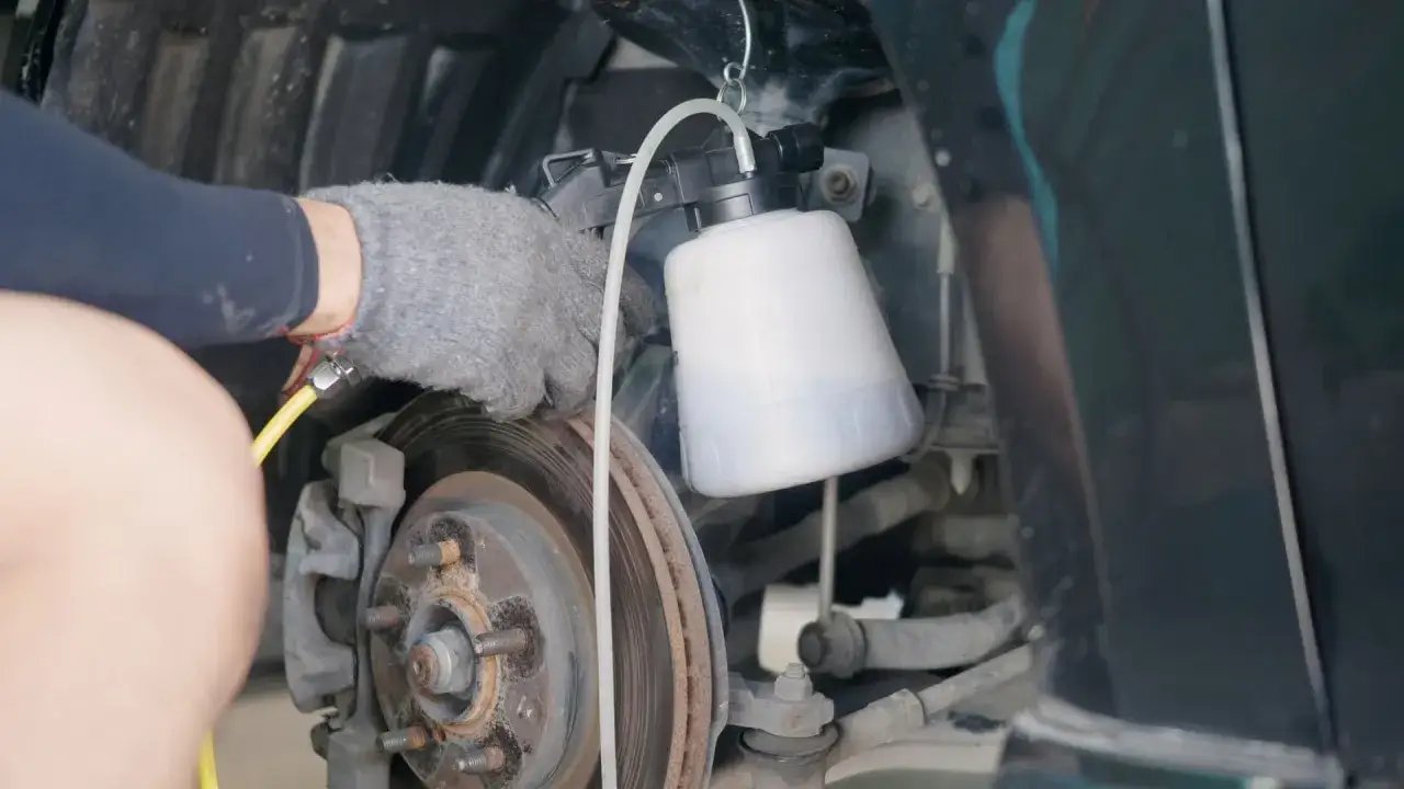 Mechanik w rękawicy wykonuje wymianę płynu hamulcowego przy użyciu specjalnego urządzenia.