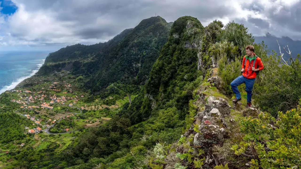 Wanderer genie&szlig;t atemberaubende Aussicht auf Madeira. Gr&uuml;ne Berge, K&uuml;ste und ein Dorf sind zu sehen. Ein Highlight f&uuml;r Madeira Sehensw&uuml;rdigkeiten.