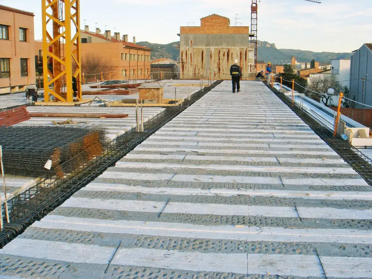 El forjado de hormigón se prepara para la construcción. Obreros supervisan la colocación de las vigas prefabricadas y el mallazo de acero.