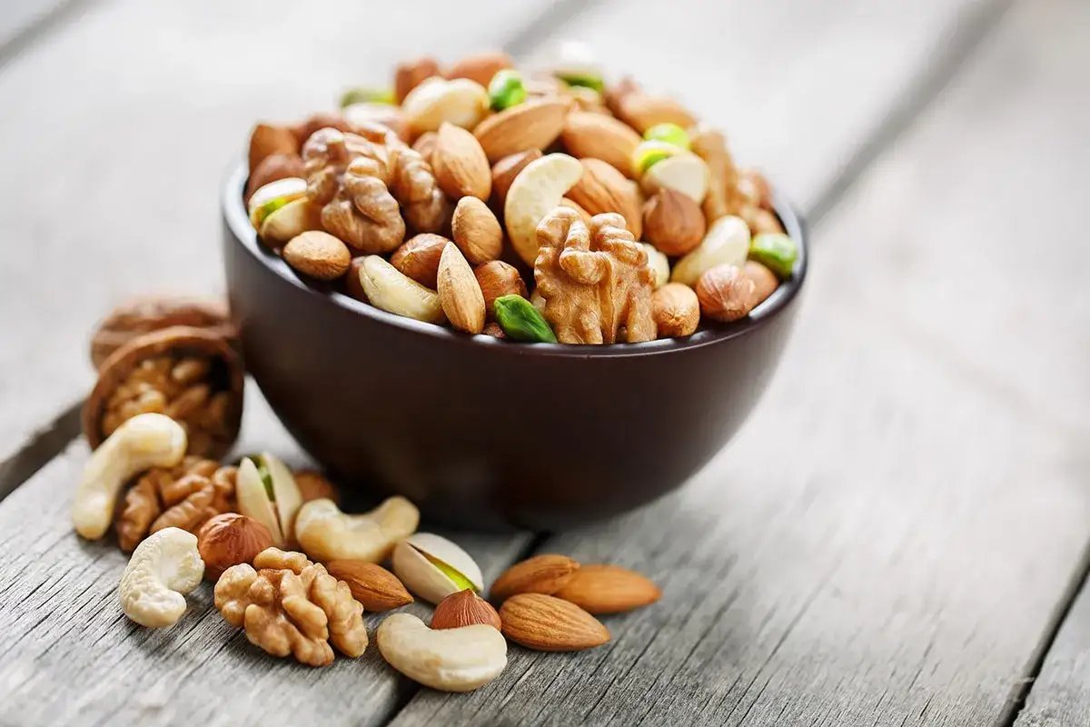 Un tazón lleno de frutos secos variados, como nueces, almendras y anacardos, descansa sobre una mesa de madera. ¡Cuidado, los frutos secos engordan!
