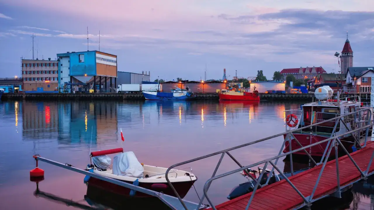 Port w Władysławowie o zmierzchu. Widać zacumowane łodzie, budynki portowe i wieżę. W oddali majaczy władysławowo molo.