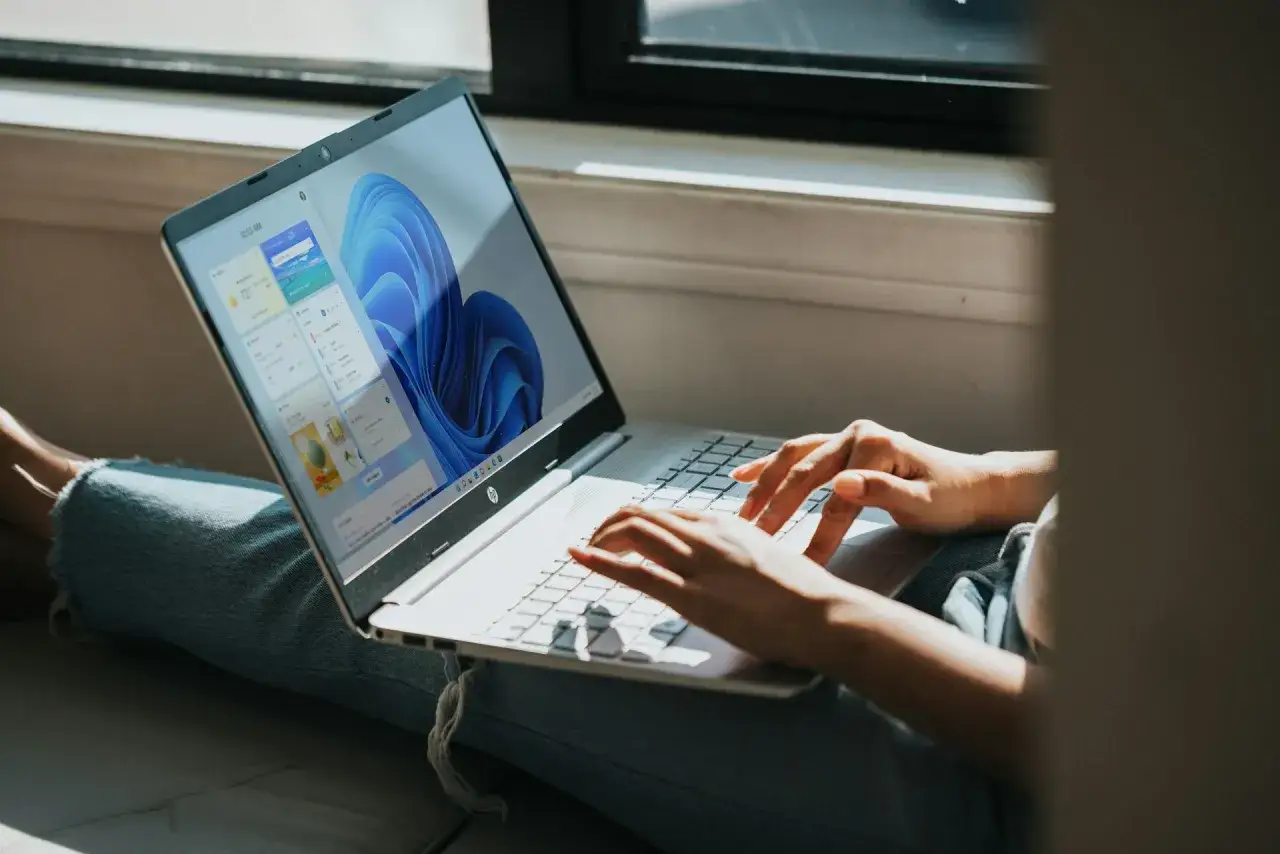 Osoba pracuje na laptopie z systemem Windows 11, wyświetlającym widżety z pogodą i wiadomościami.