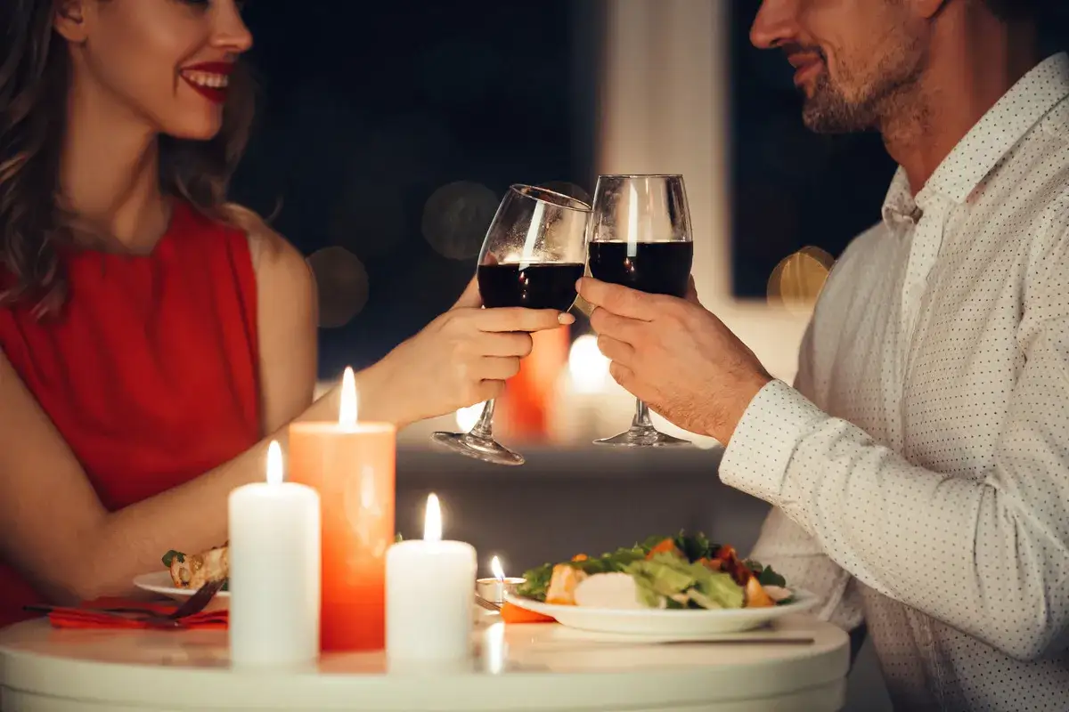 Romantyczna kolacja przy świecach. Para wznosi toast kieliszkami czerwonego wina, uśmiechając się do siebie.