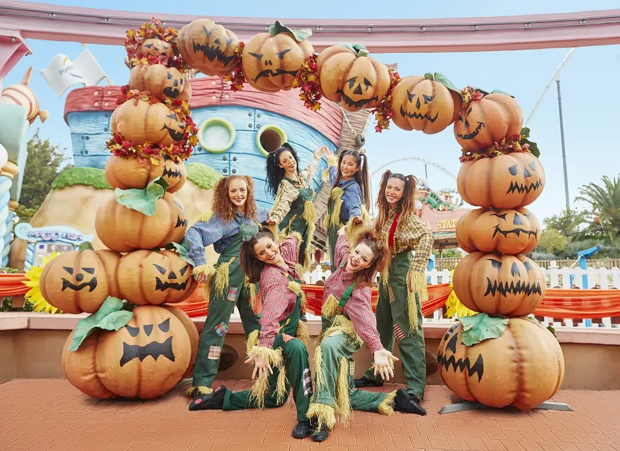 Animadoras con disfraces de espantapájaros posan junto a calabazas gigantes en PortAventura Halloween.