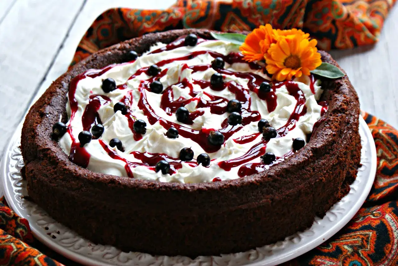 Pyszny brownie z fasoli, udekorowane bitą śmietaną, polewą z czarnej porzeczki i świeżymi owocami.