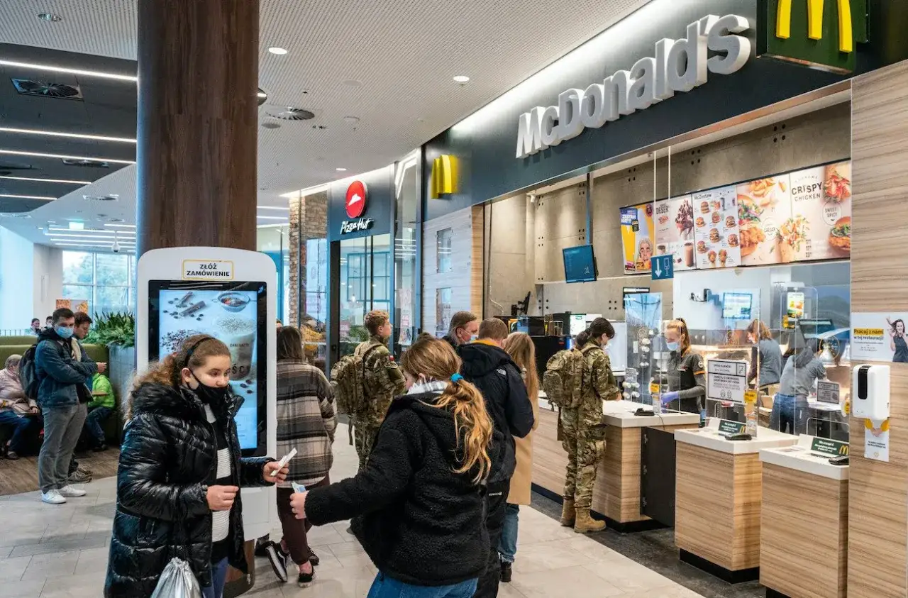 Ludzie w kolejce do McDonald's, zastanawiają się, ile się zarabia w maku, podczas gdy pracownicy obsługują klient&oacute;w.