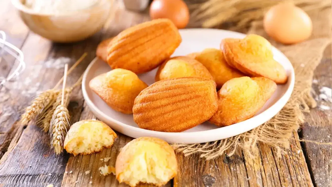 Assiette de madeleines dorées, parfaites pour une recette madeleine moelleuse. Des épis de blé et des œufs rappellent les ingrédients frais.