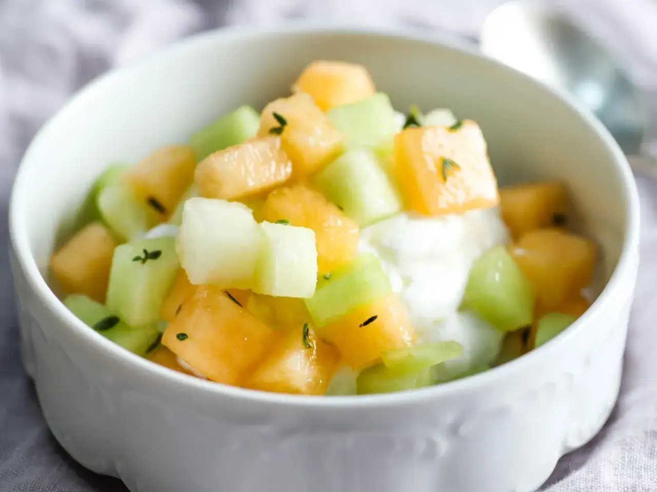 Schüssel mit Honigmelone und Cantaloupe-Würfeln auf Joghurt, garniert mit Kräutern. Ein gesunder Genuss!