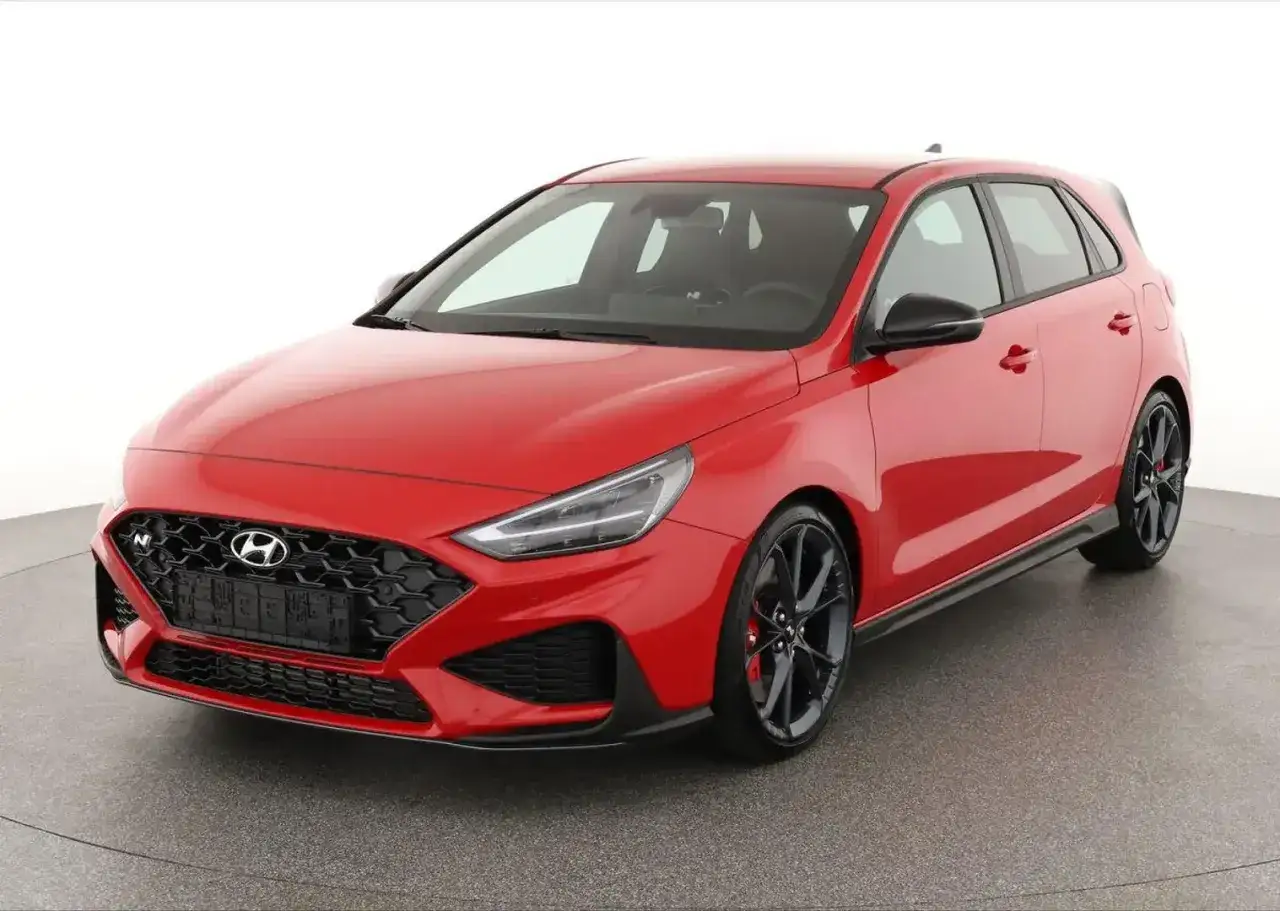 Czerwony Hyundai i30 N, sportowy hatchback z czarnymi felgami i agresywnym grillem, gotowy na wyścigi.