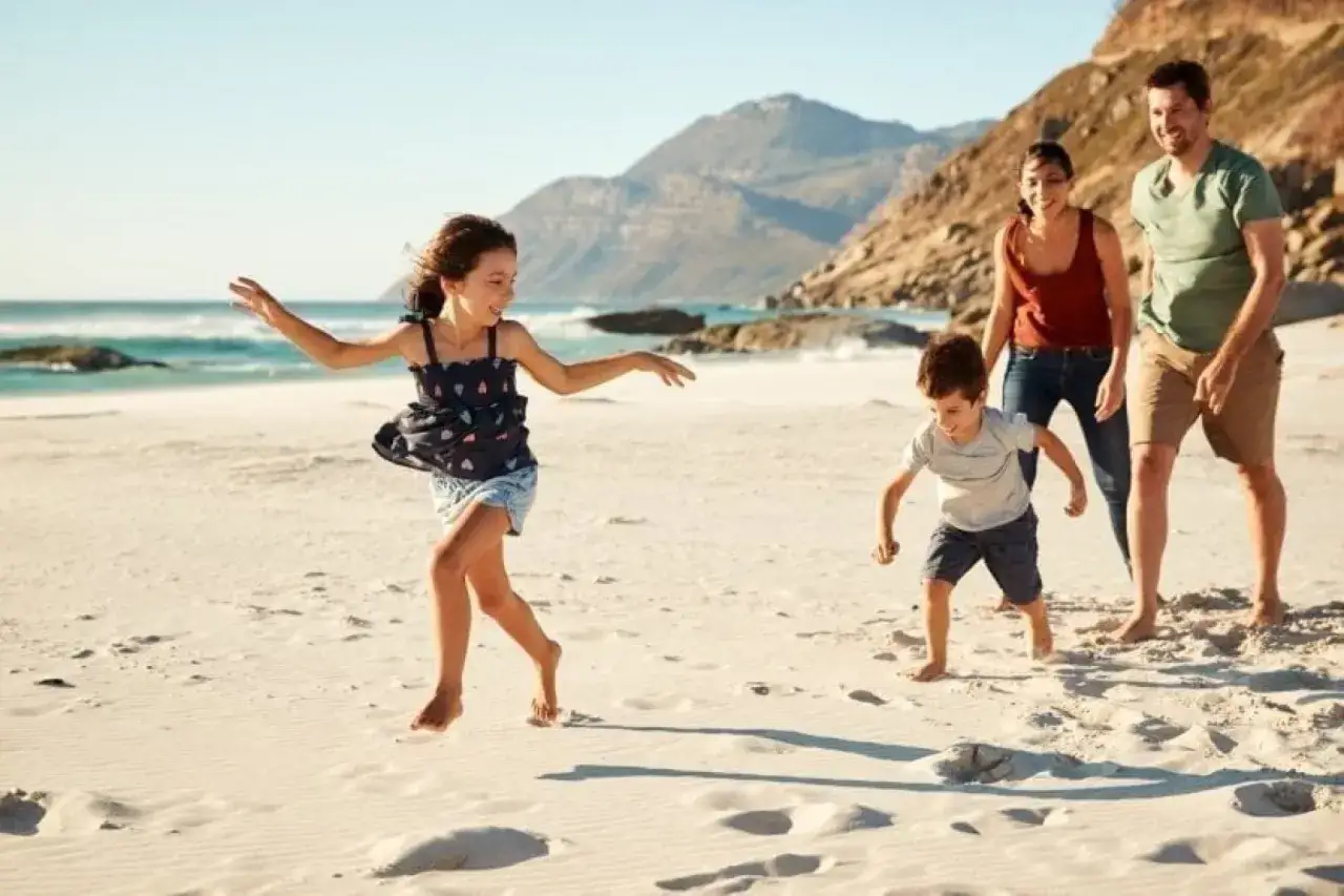 Une famille profite de sa vacance en famille sur une plage ensoleillée, les enfants courent joyeusement sur le sable tandis que les parents les regardent avec un sourire.