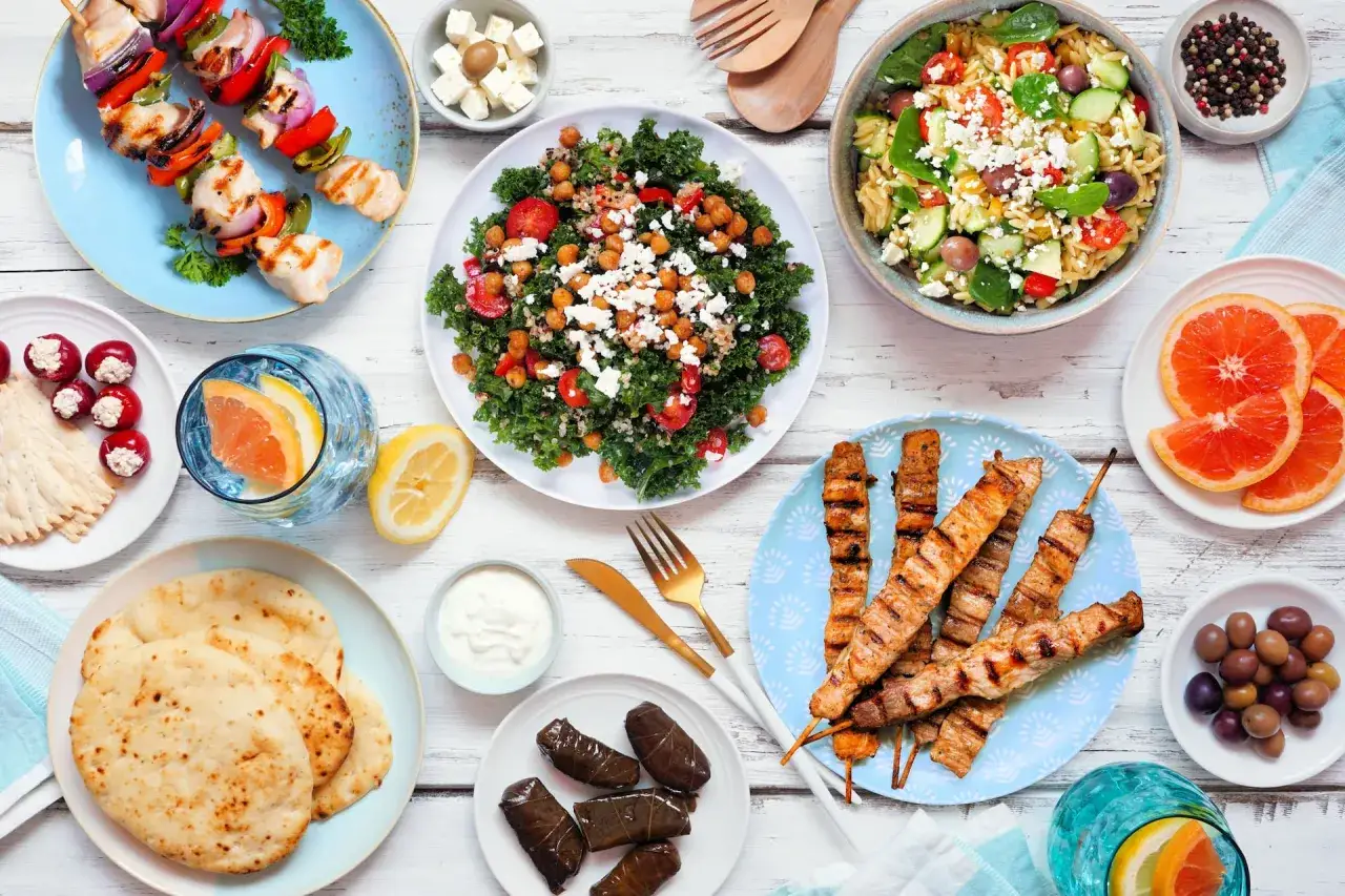 Mesa con brochetas de pollo, ensalada de kale con garbanzos y queso feta, y pinchos de carne. Una comida rica en proteínas vegetales y otros ingredientes frescos.