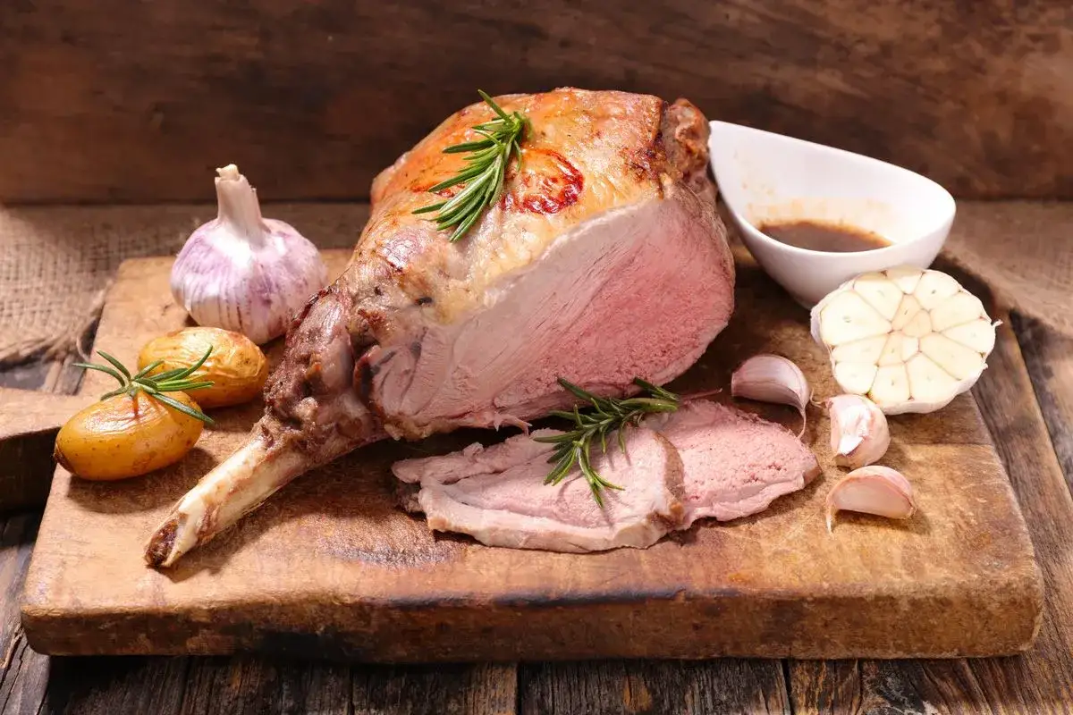 Gigot d'agneau rôti, parfait pour une recette agneau pascal. Servi avec des pommes de terre, de l'ail et du romarin.