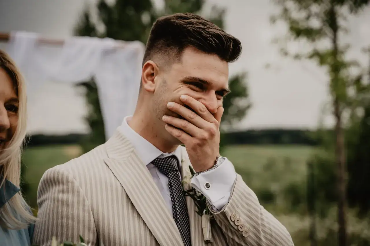 Novio con peinado impecable, cubri&eacute;ndose la boca con emoci&oacute;n durante la boda.