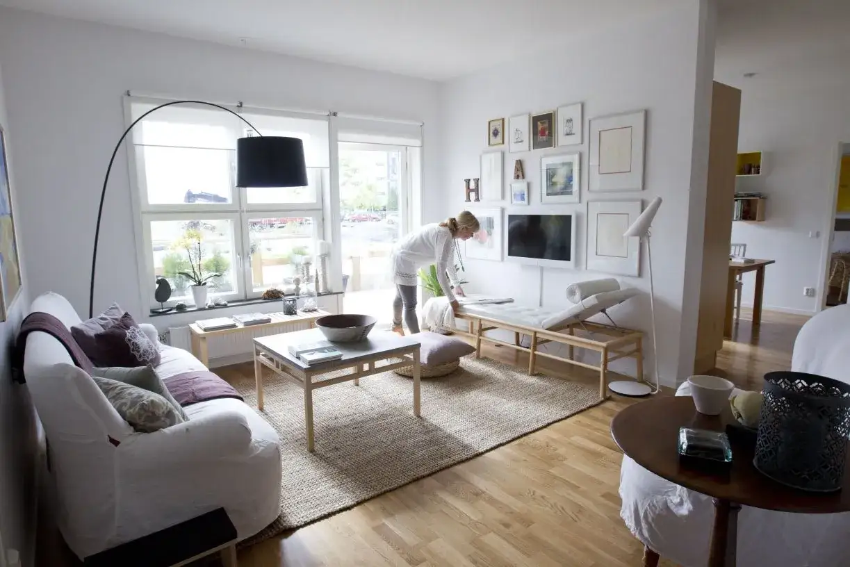 Ett ljust och luftigt vardagsrum med vita möbler, en stor matta och en kvinna som ordnar. En känsla av lugn och harmoni, som i ett feng shui vardagsrum.