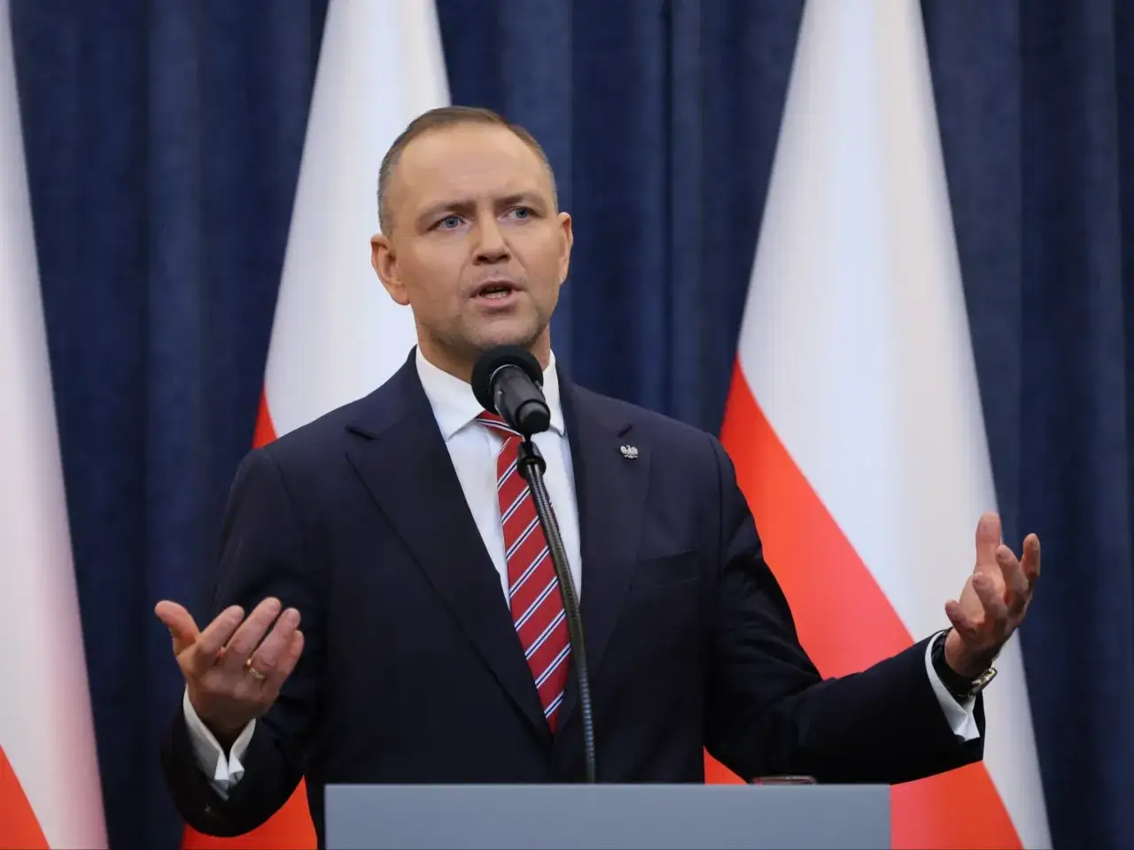 Mężczyzna w garniturze przemawia przy mikrofonie na tle flag. Czy prezydent planuje powołanie nowej rady konsultacyjnej z udziałem młodych liderów?