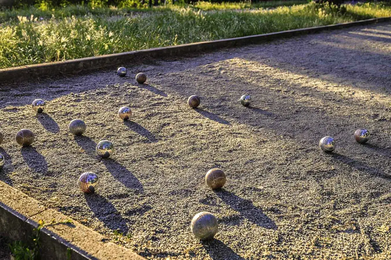 Terrain de p&eacute;tanque avec des boules dispers&eacute;es sur le sable. Le soleil couchant projette de longues ombres. Quel sable pour terrain de p&eacute;tanque ? Un sable fin et bien tass&eacute;.