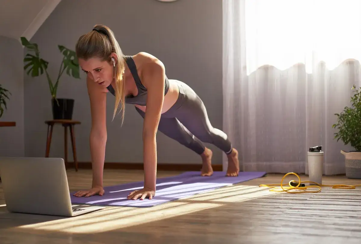 Kobieta ćwiczy w domu, wykonując pozycję deski przed laptopem. Czy to trening hiit?