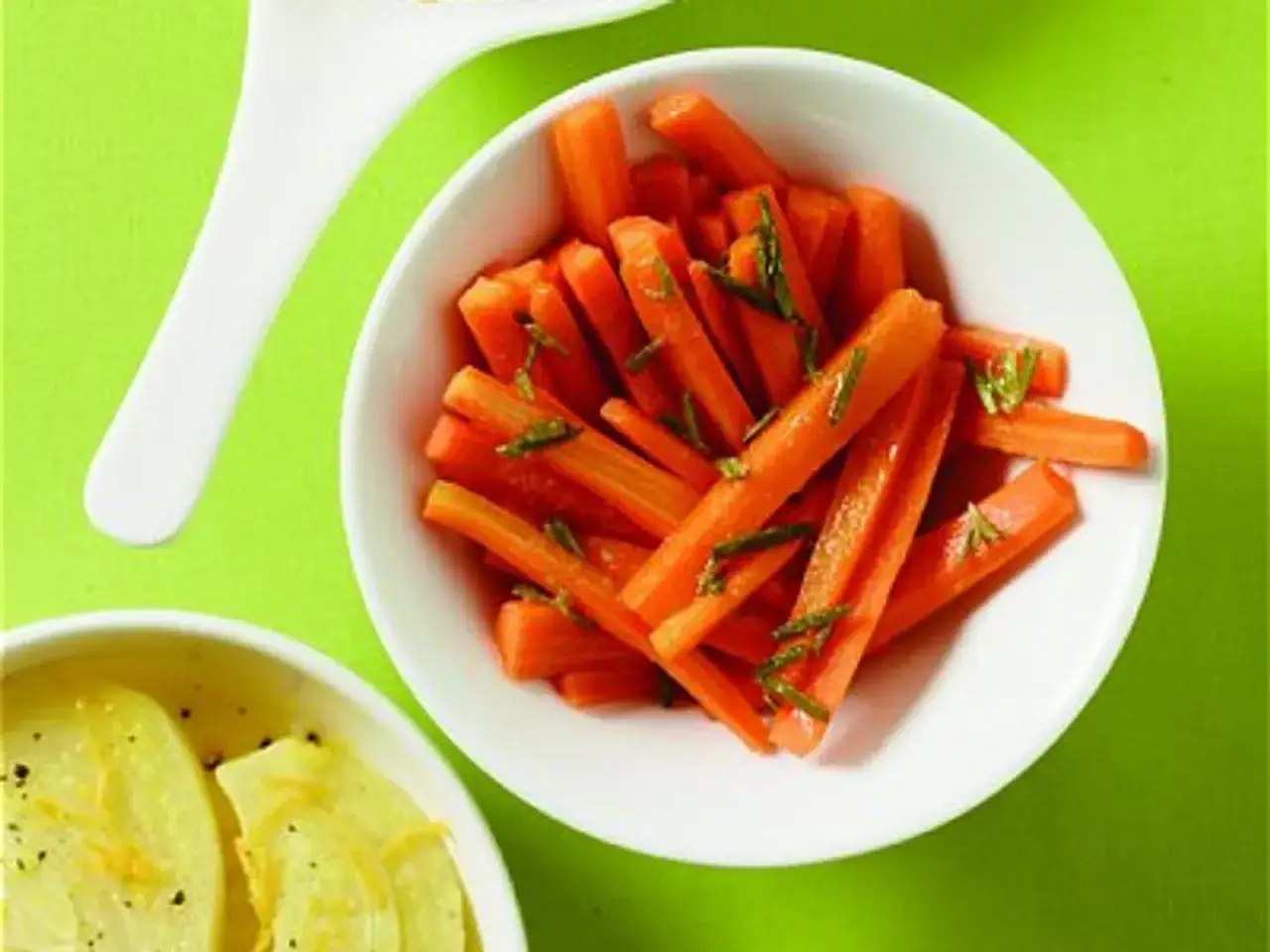 Carottes à la marocaine, coupées en bâtonnets et parsemées d'herbes fraîches, dans un bol blanc sur fond vert vif.