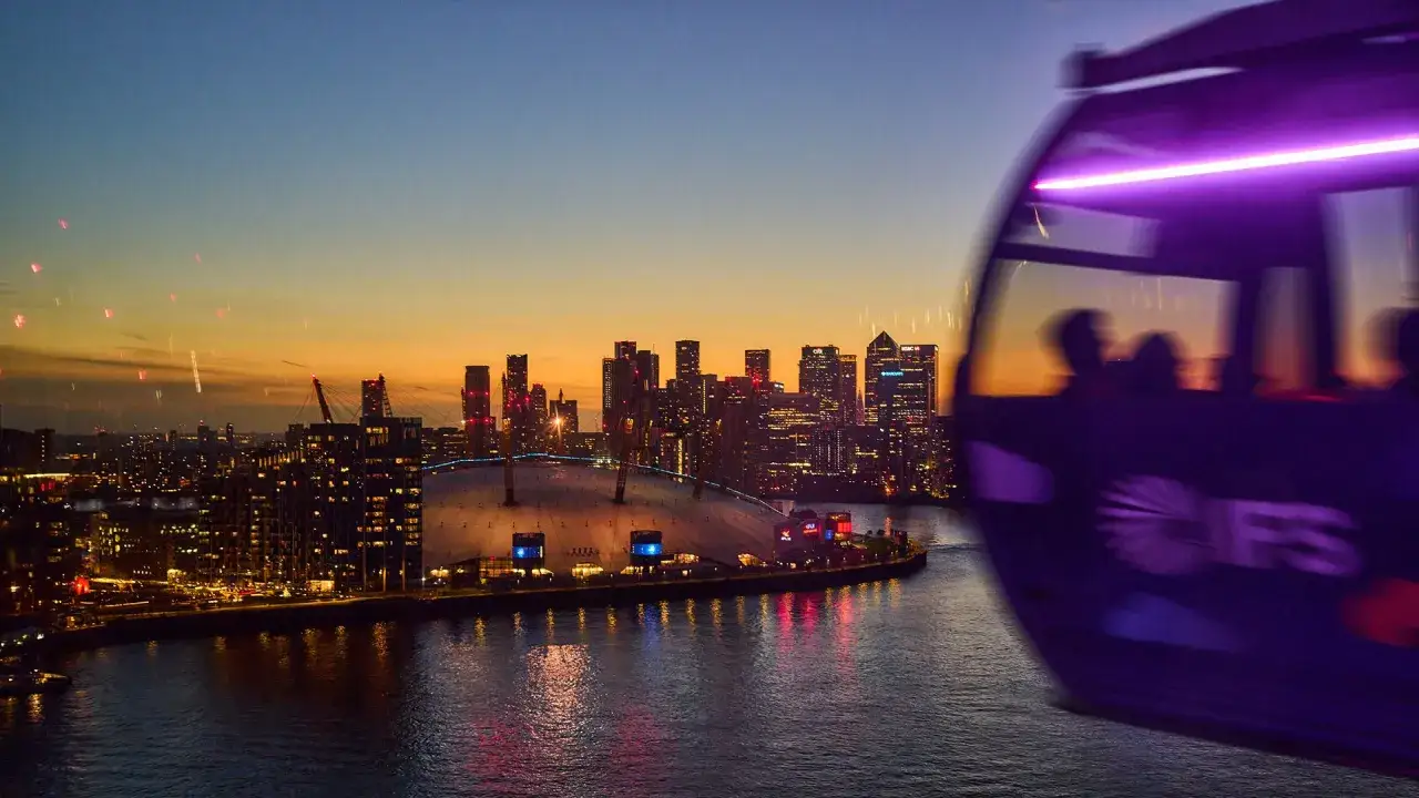 En linbana i London glider fram &ouml;ver en stad i skymningen. Silhuetter av skyskrapor lyser upp horisonten.