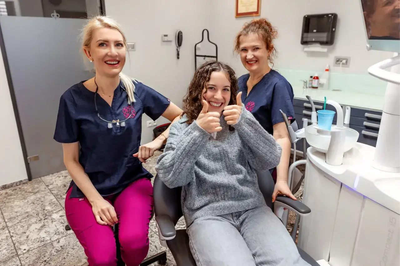 Uśmiechnięta pacjentka z dwiema dentystkami. Pokonany strach przed dentystą, radość i kciuki w g&oacute;rę.