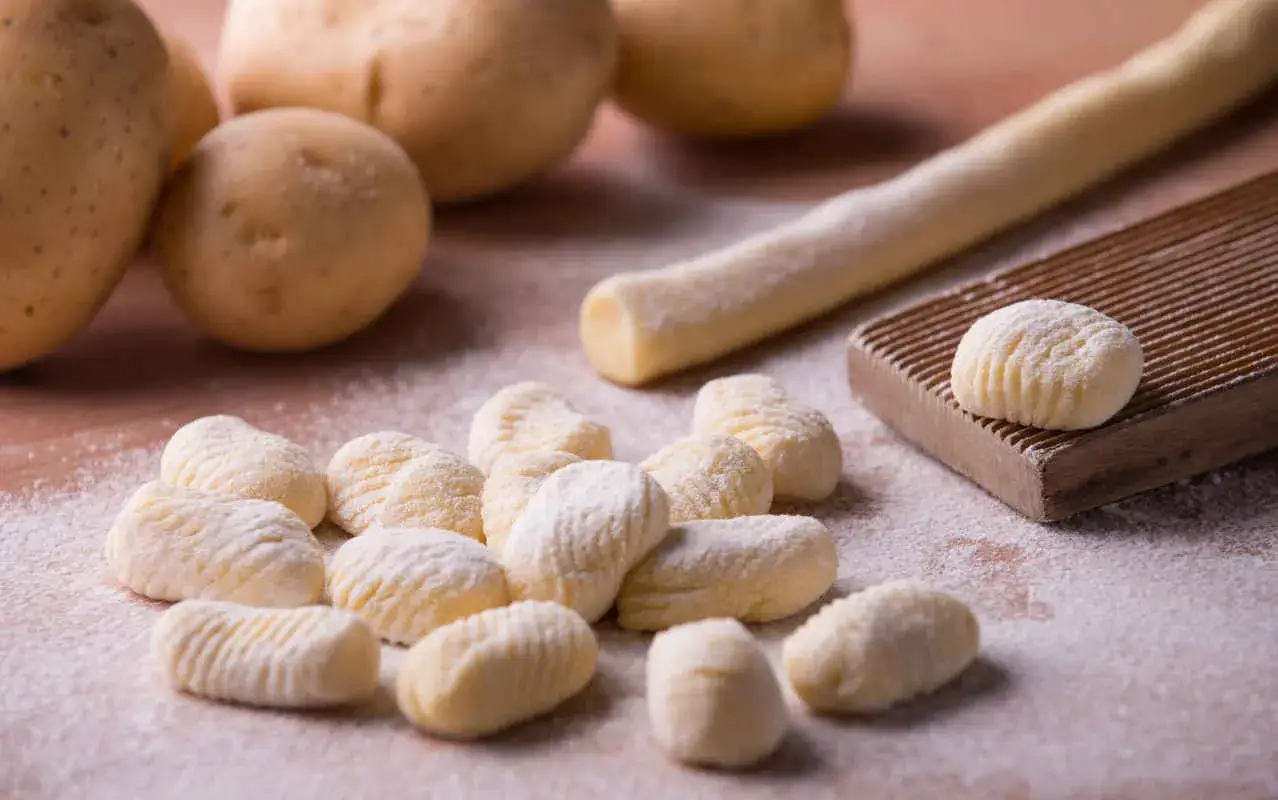 Patate e gnocchi fatti in casa pronti per essere cucinati. Un'immagine che mostra come cucinare gli gnocchi, con ingredienti freschi e attrezzi da cucina.