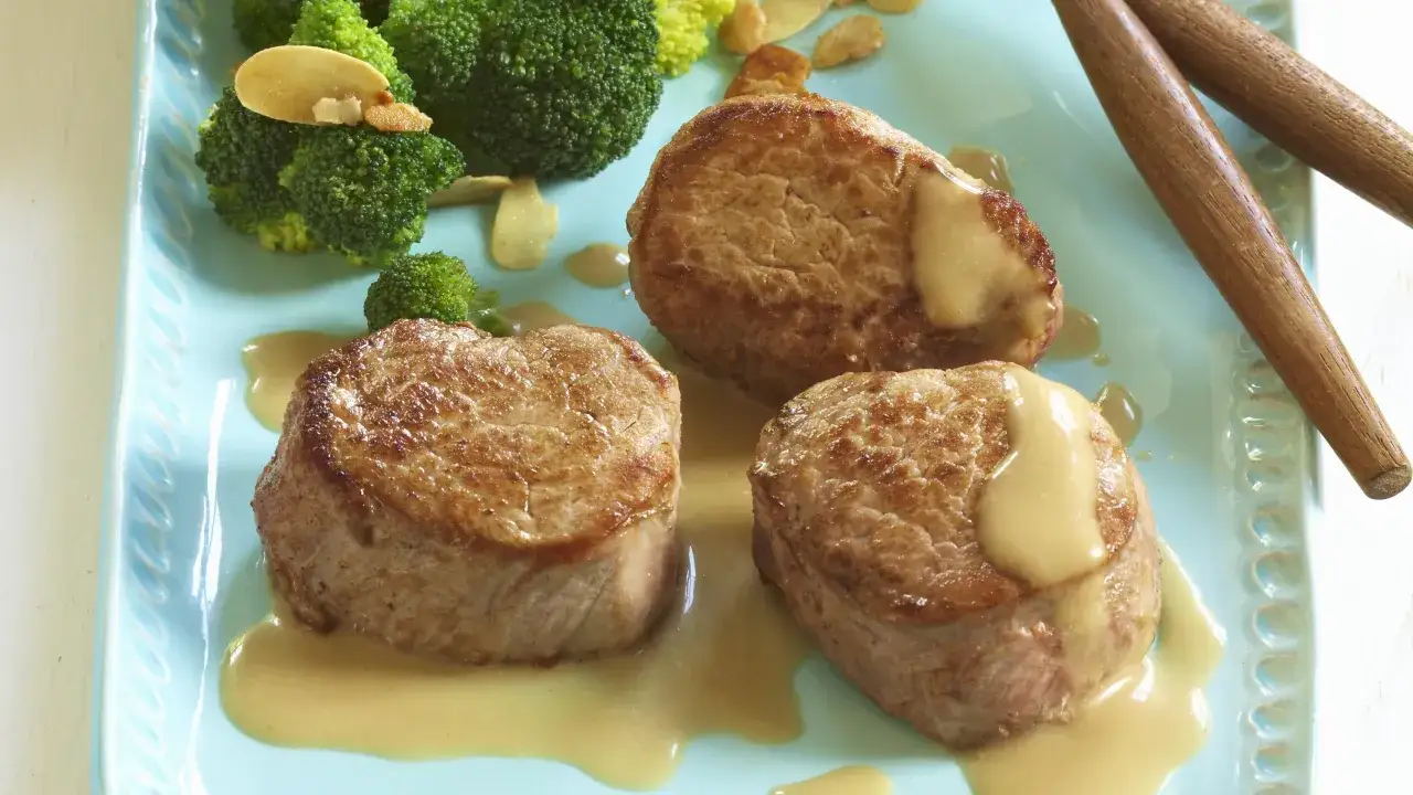 Trois médaillons de porc nappés de sauce, accompagnés de brocolis et d'amandes effilées. Une belle présentation pour une recette médaillon de porc.