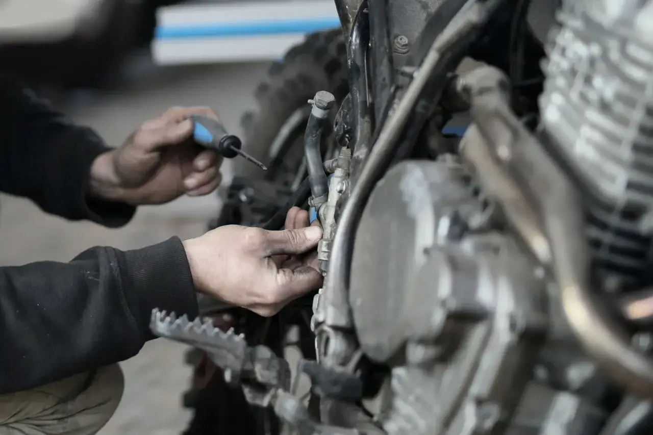 Mec&aacute;nico revisa la moto, buscando la causa de por qu&eacute; se ahoga la moto, ajustando una pieza del motor con un destornillador.