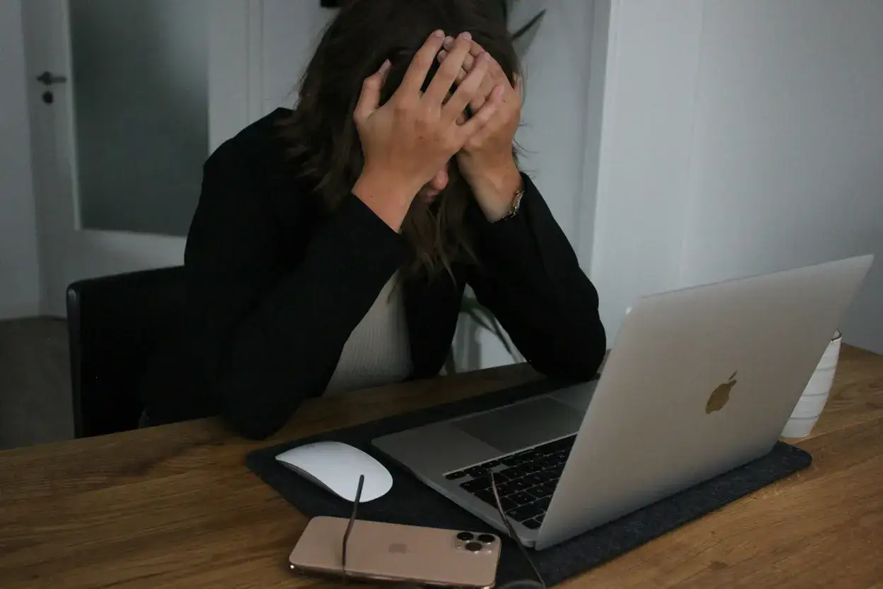 Zestresowana kobieta z rękami na twarzy przy laptopie. Czy groźby są karalne? Zastanawia się nad tym, przeglądając coś w internecie.