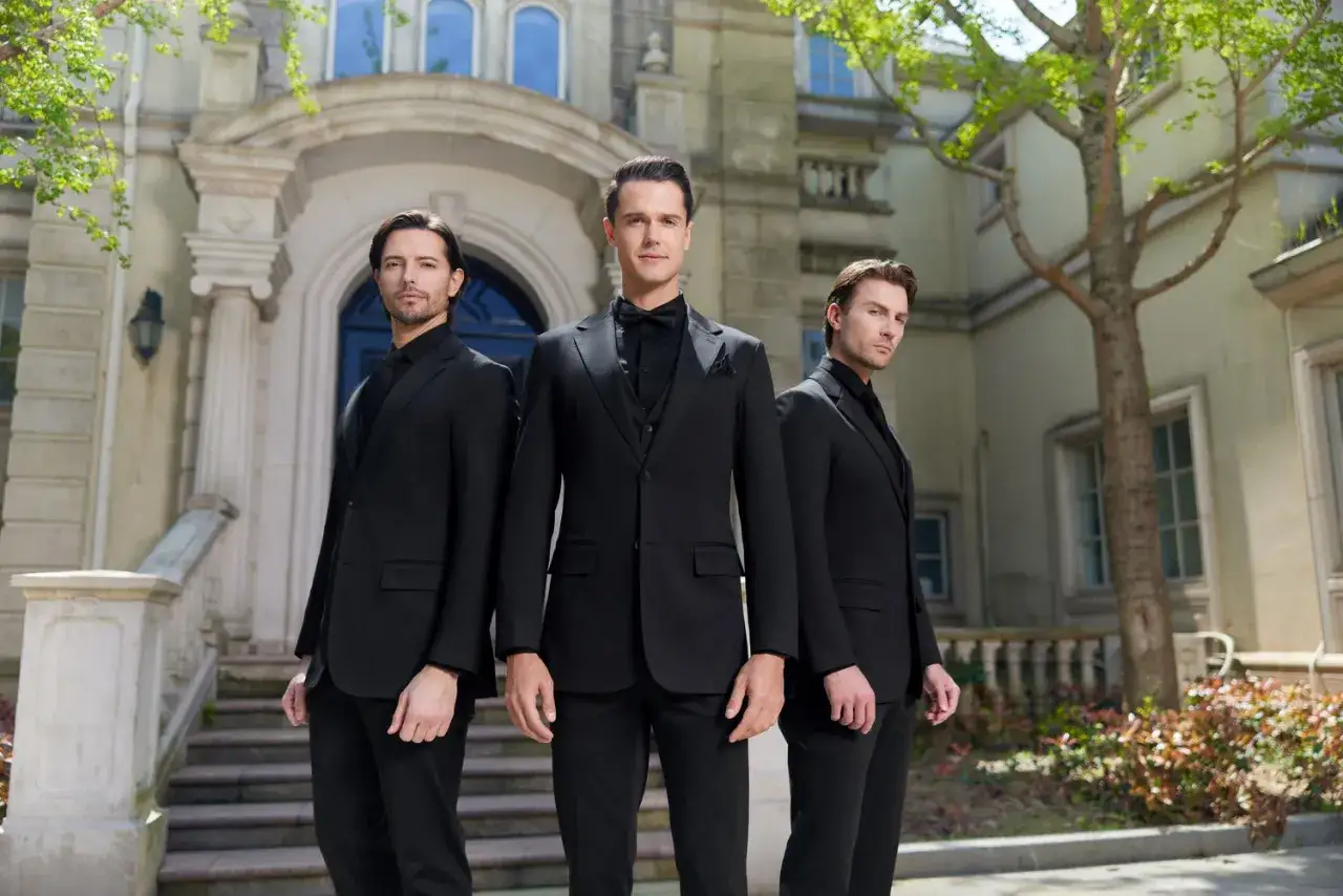 Three men in sharp black suit ideas stand before a grand building.