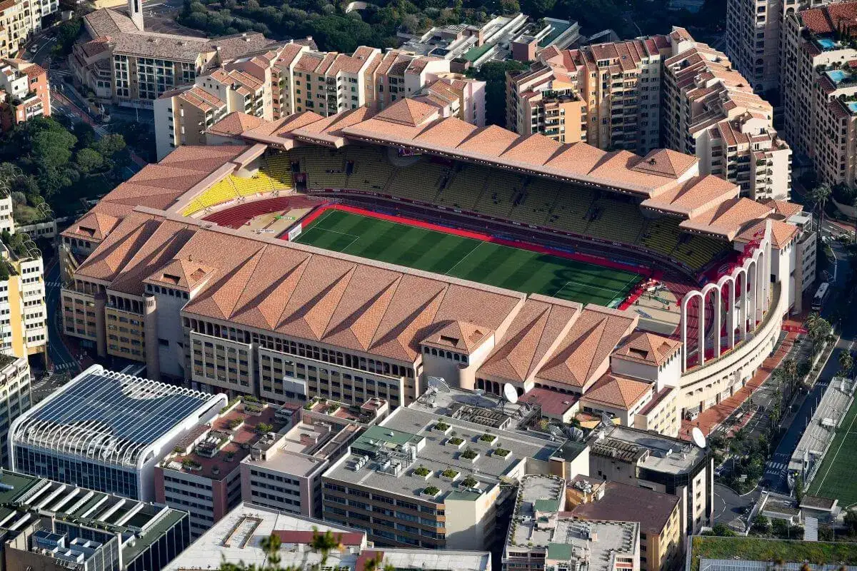 Stadion Louis II w Monako, dom AS Monaco FC, z lotu ptaka. Widok na zieloną murawę, żółte trybuny i otaczające budynki.