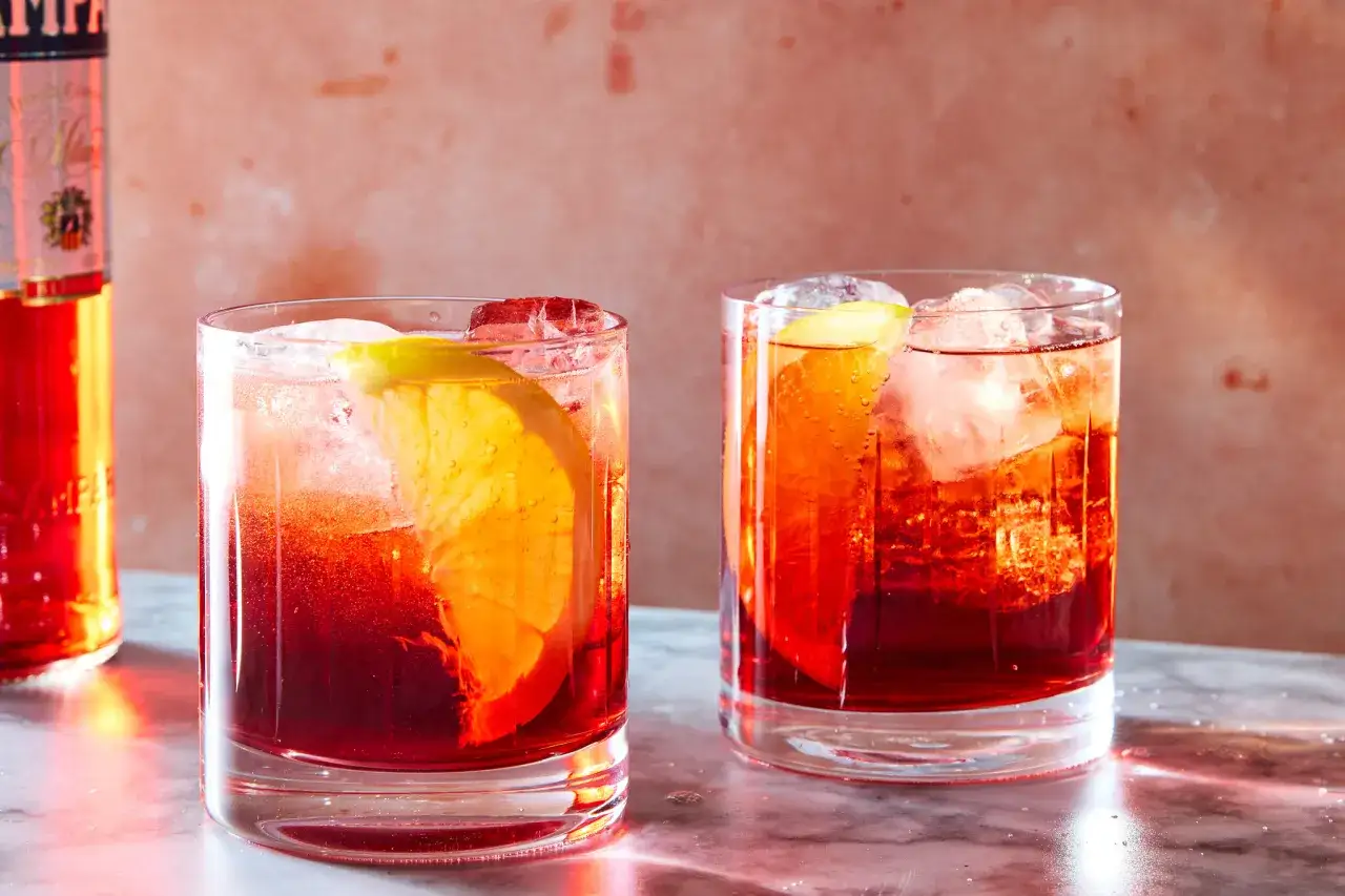 Dwa orzeźwiające drinki Negroni Sbagliato z pomarańczą i lodem, obok butelki Campari. Idealny przepis na lato.