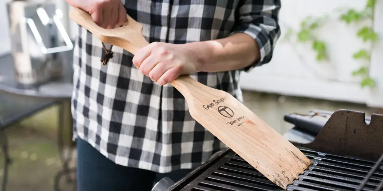 Persona usa un raspador de madera para limpiar parrilla barbacoa oxidada.