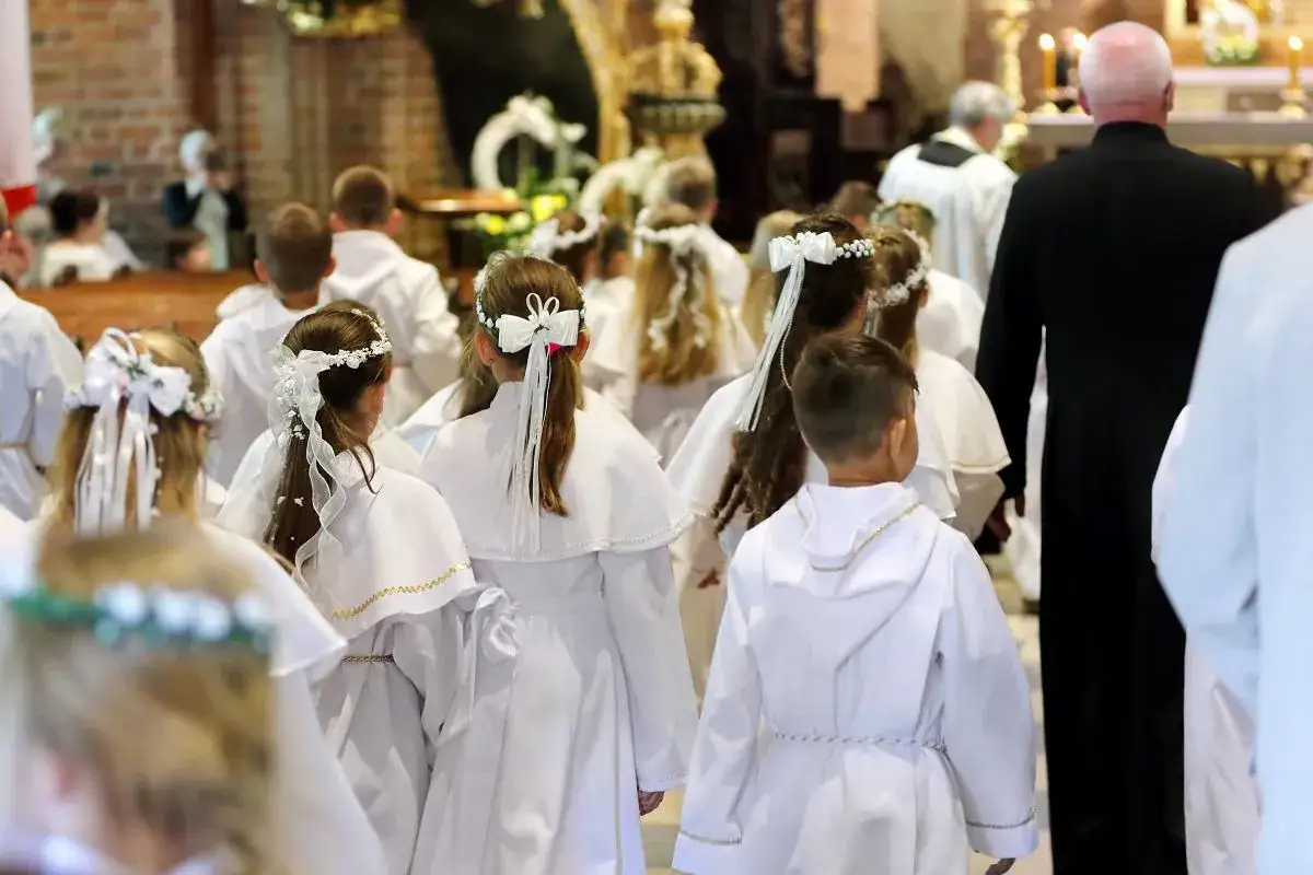 Dzieci w białych strojach, zazwyczaj w wieku około 9 lat, idą do komunii w kościele.