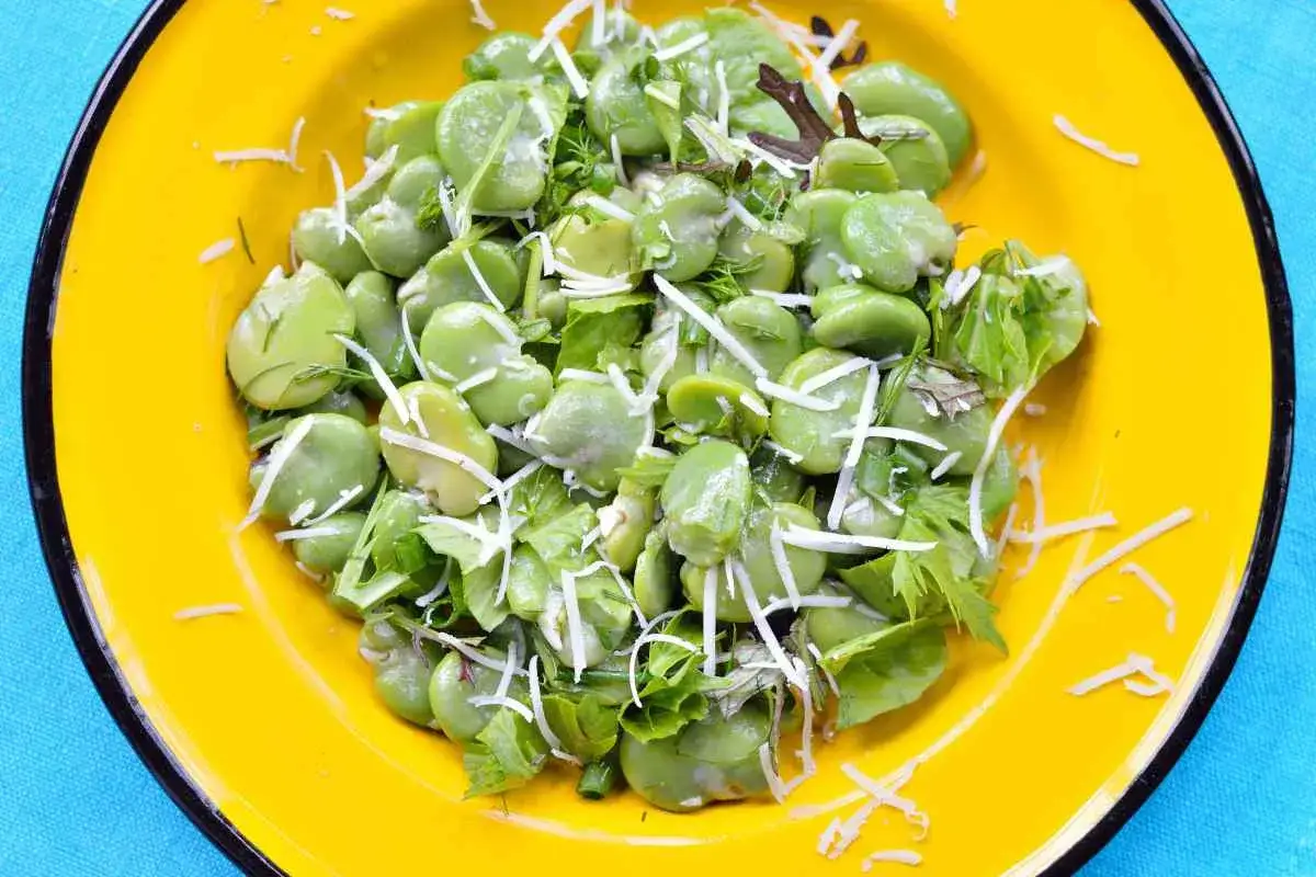 Fave fresche e ricotta grattugiata su un piatto giallo, un'esplosione di sapori primaverili.