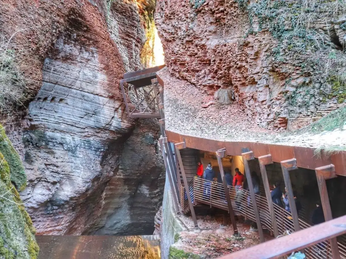 Persone percorrono una passerella metallica lungo le pareti rocciose di un canyon, vicino al ponte dell'orrido.