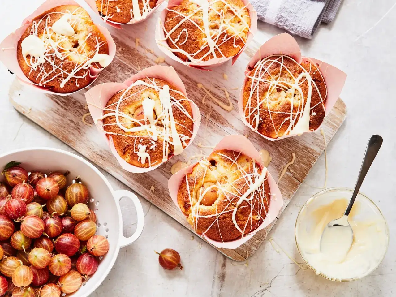 Saftige stachelbeer muffins, mit weißer Schokolade verziert, warten neben frischen Stachelbeeren auf den Genuss.