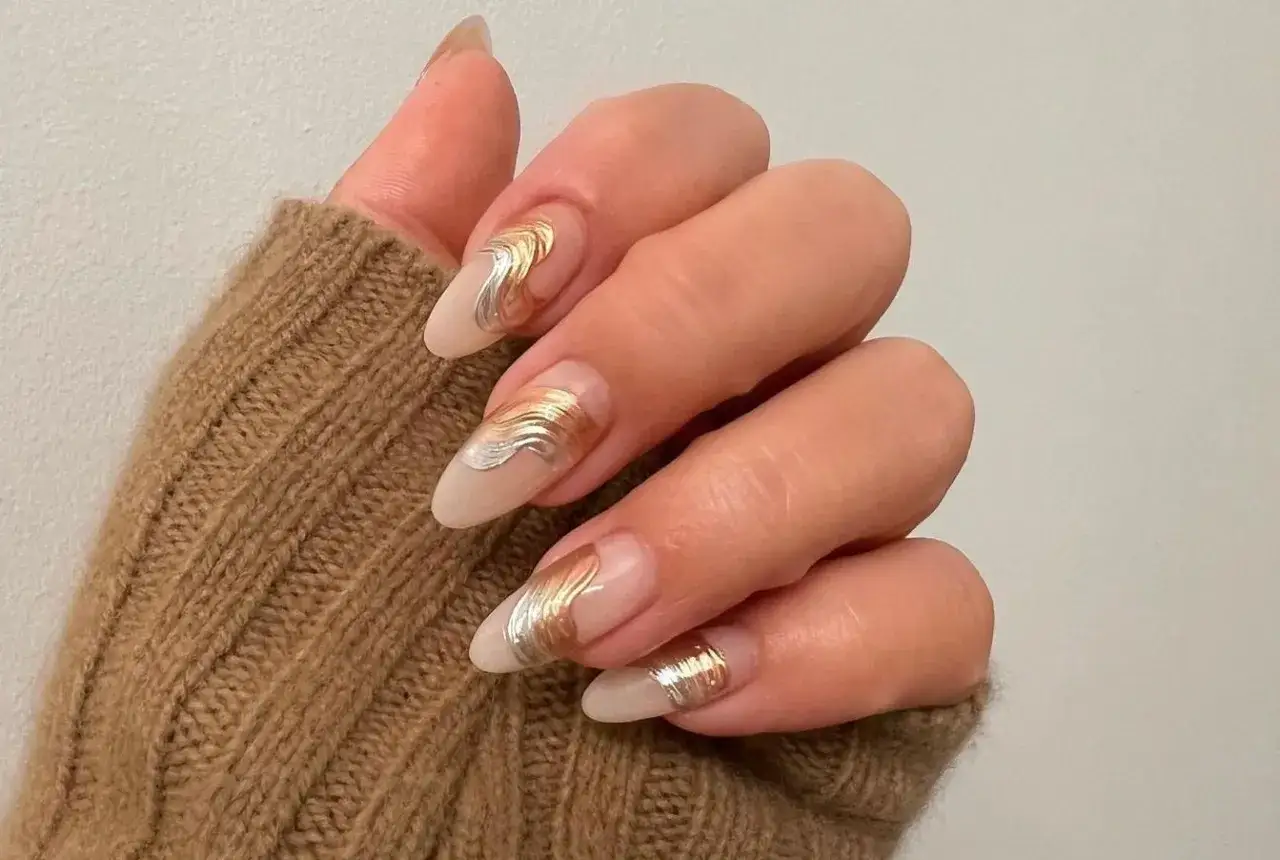 Manucure élégante avec un dessin ongles gel or et argenté, rappelant des vagues métalliques sur une base nude.
